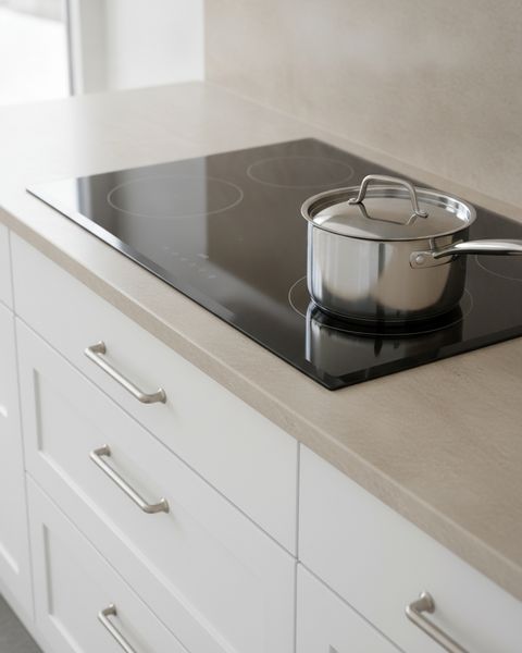 A black glass induction cooktop set into a stone countertop, a saucepan on one zone