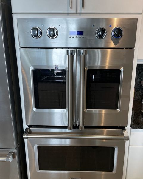 A stainless French-door double wall oven built into white cabinets