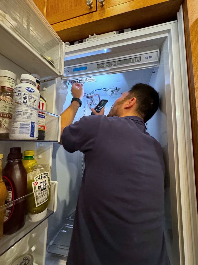 A technician working at the open control housing at the top of a panel-ready built-in refrigerator, wood cabinets around it