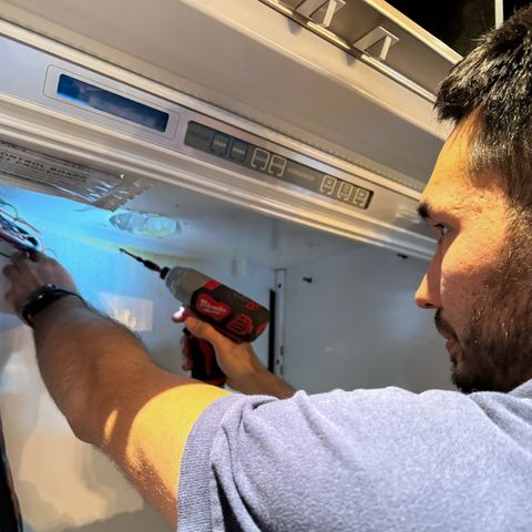 A technician driving a screw into the control housing of a built-in refrigerator with a cordless driver