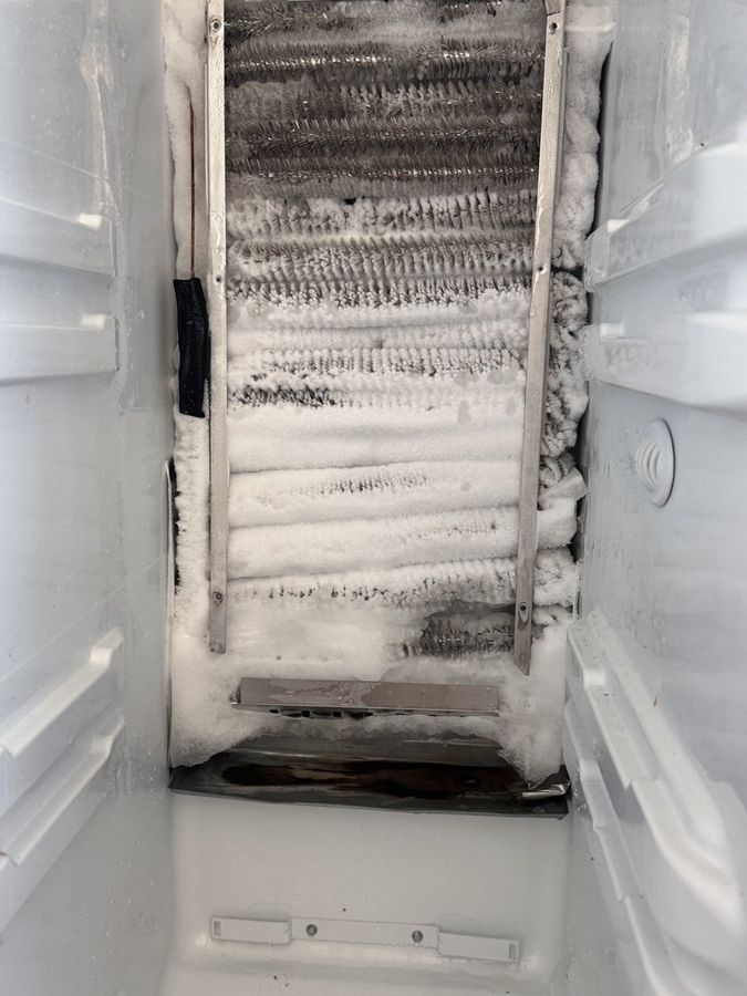 The back of a freezer with its panel off, the evaporator coil packed solid with frost
