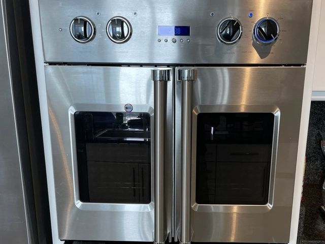 A stainless French-door double wall oven built into white cabinets