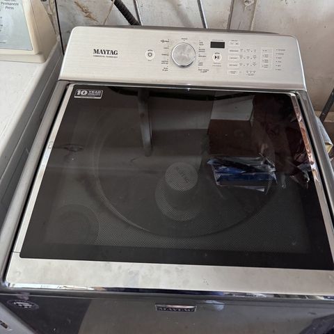 A top-load washer under the water valves of a utility room wall