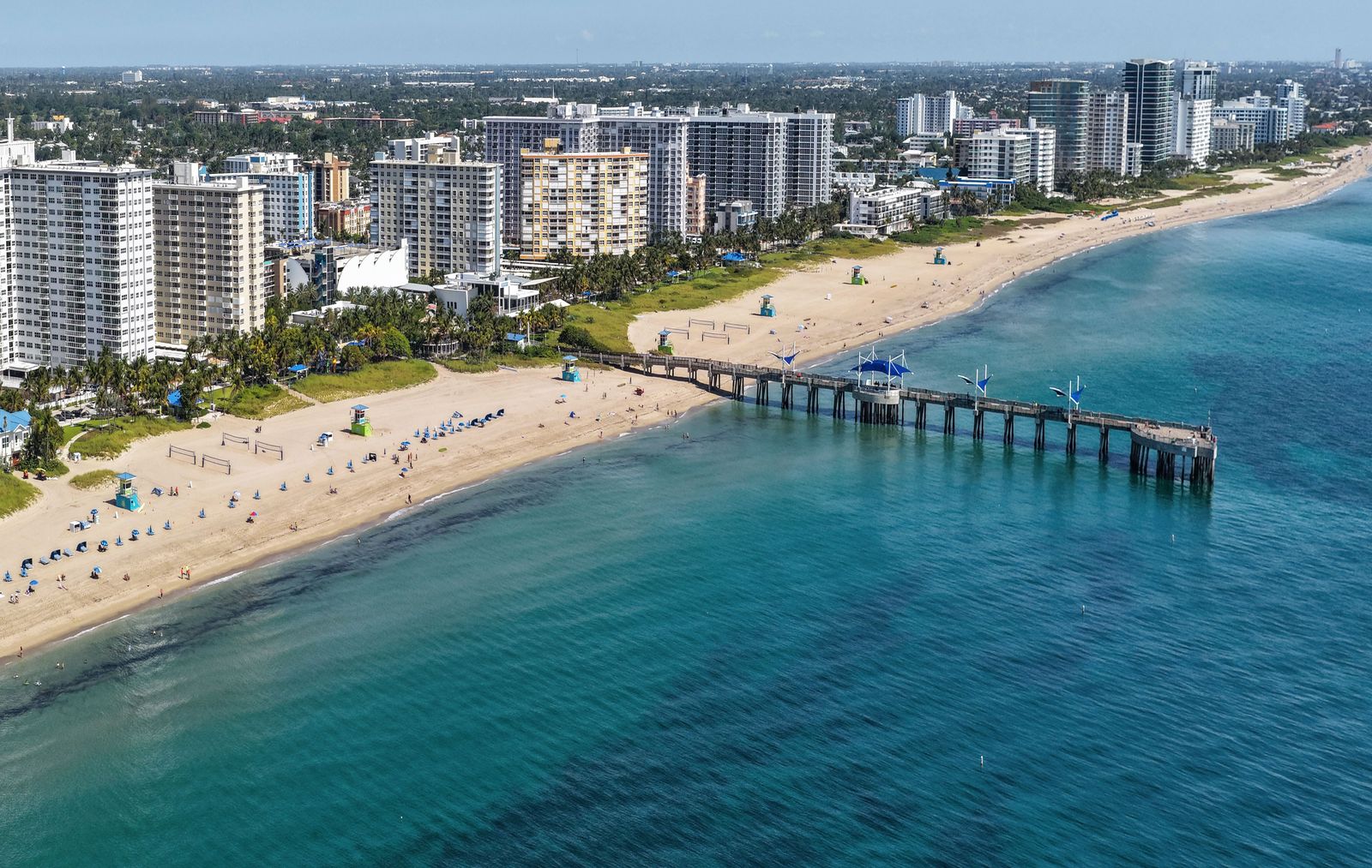 Aerial view looking north along Pompano Beach: condo towers behind the sand and the Fisher Family Pier reaching out over turquoise water