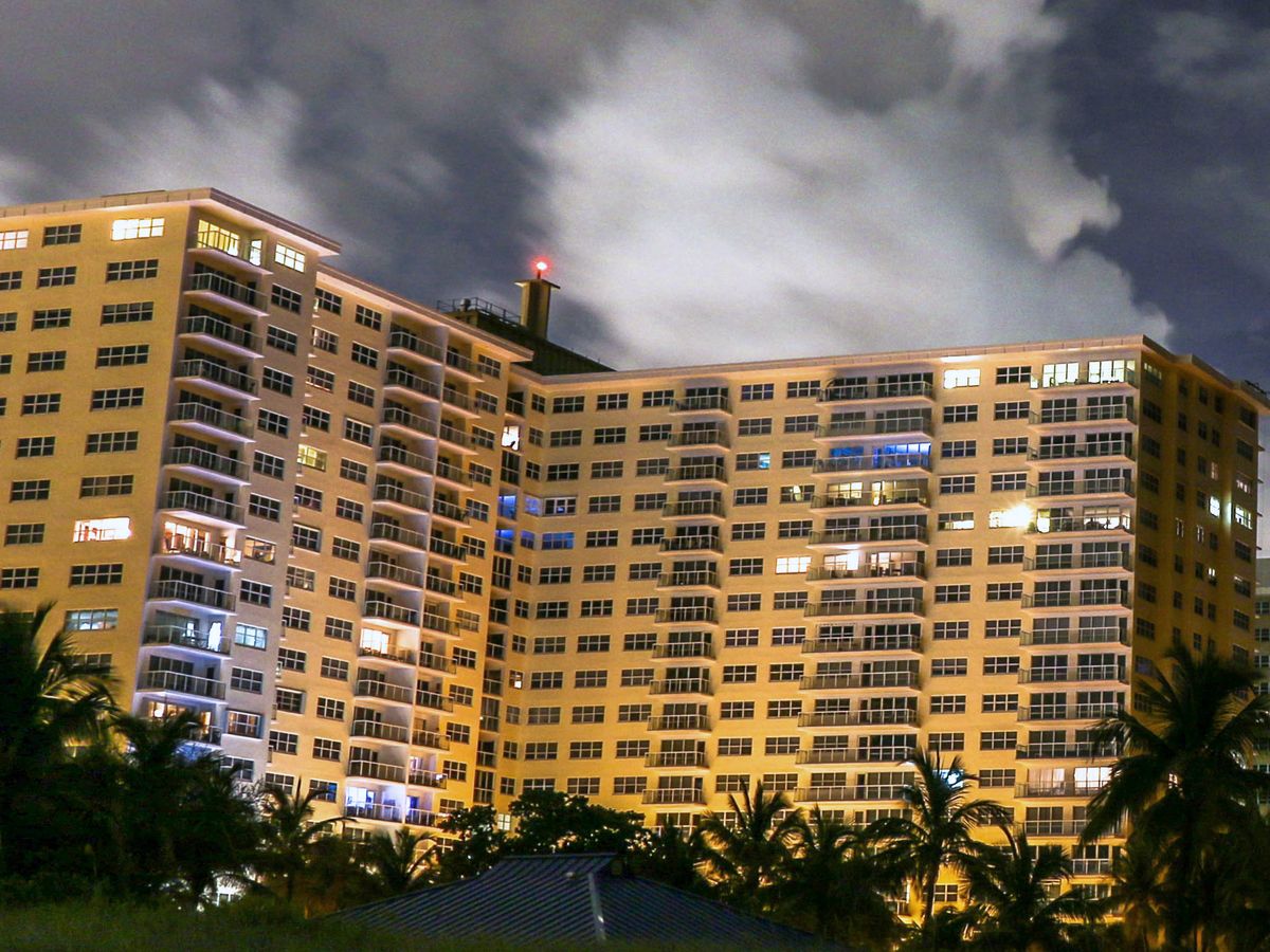 Condo towers lit up at night behind palms and the dune, seen from the sand on Pompano Beach