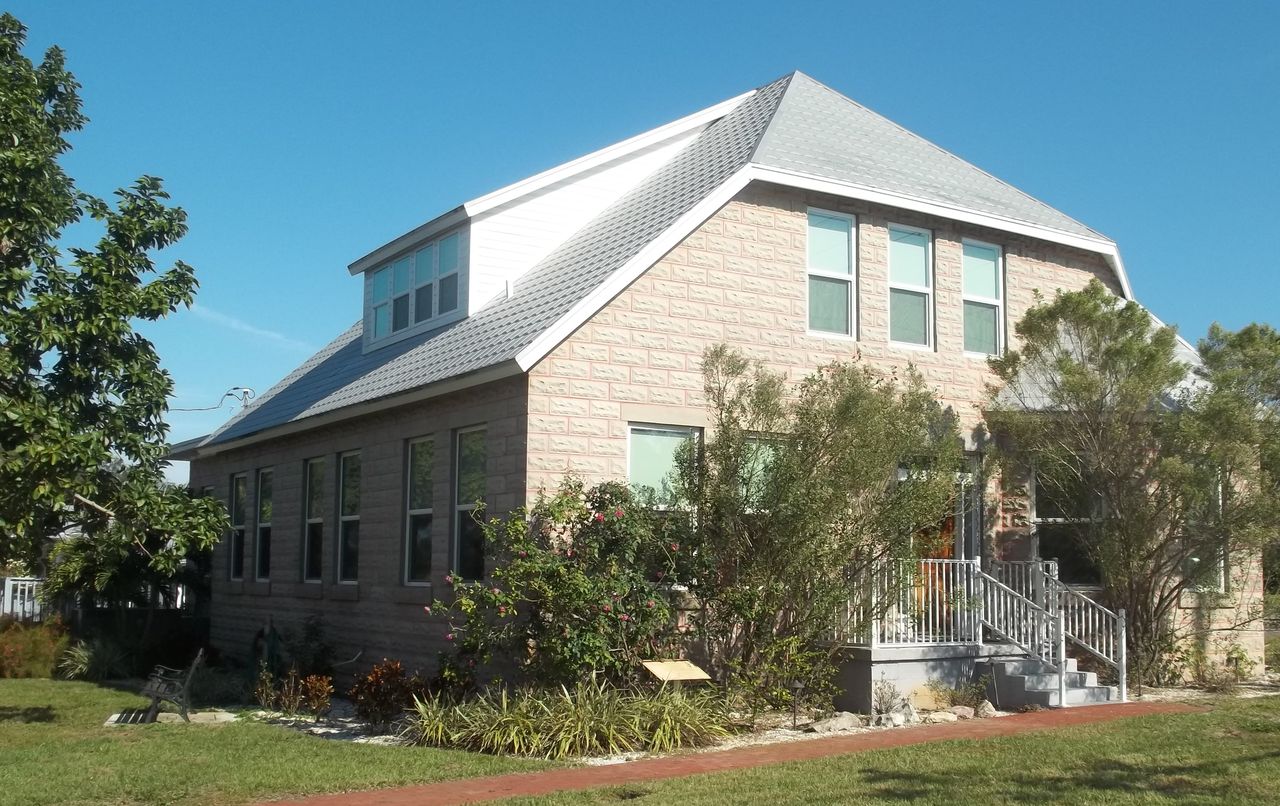 The Palm Harbor Museum, a two-storey block house with a grey hip roof and dormer, porch steps and a lawn with a brick path