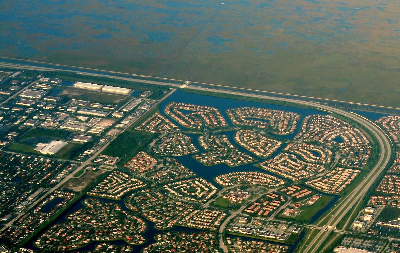 The Sawgrass Expressway curving between Parkland and Coral Springs, lake communities of tile-roof houses beside it and the open Everglades beyond