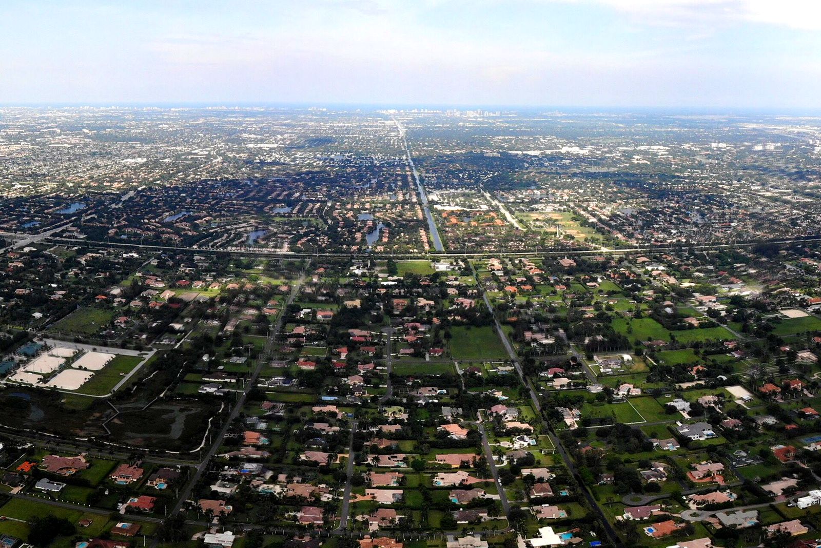 Looking east over the big lots of west Plantation from the air: houses with pools set far apart on green land, the suburb running flat to the horizon