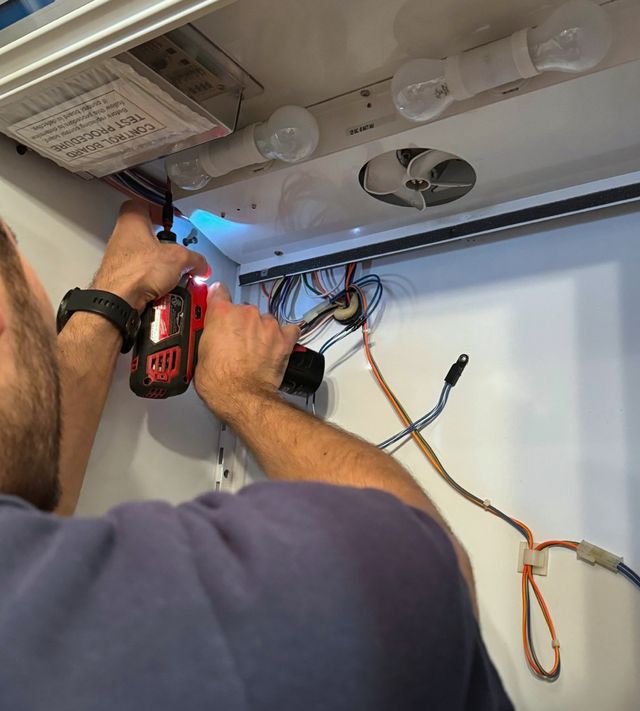 A technician with a cordless driver at the control board inside a refrigerator