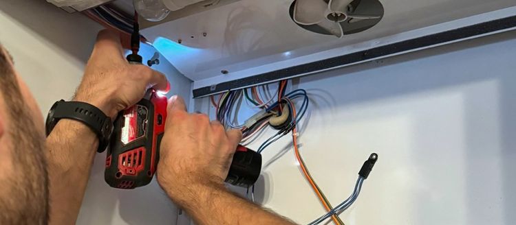 A technician’s hands with a cordless driver at a refrigerator’s control board
