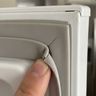 A fingertip on the corner of a refrigerator door seal that has pulled away from the door