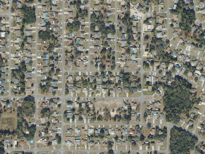 Streets of houses on lots of much the same size in Spring Hill, seen from above, with pools, driveways and trees