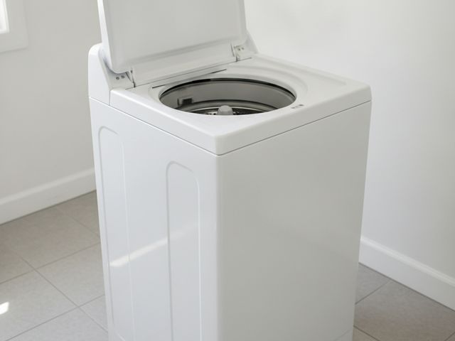 A white top-load washing machine with its lid open on a tiled floor