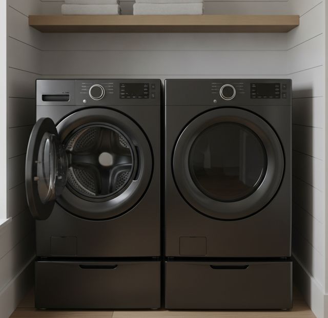 A matching dark washer and dryer side by side on pedestal drawers in a white laundry nook, the washer’s door open