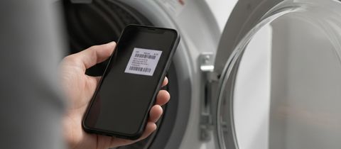 A phone held up inside the open door of a front-load washer, its screen showing a photo of the label