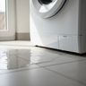 A puddle of water on a tile floor in front of a white washer