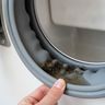 A fingertip folding back a front-load washer’s door seal to show grime in the fold