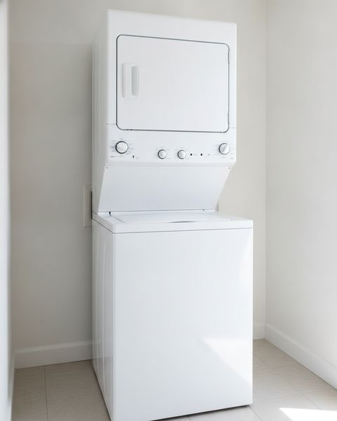 A tall white laundry center with a dryer door in its upper half and a top-loading washer below