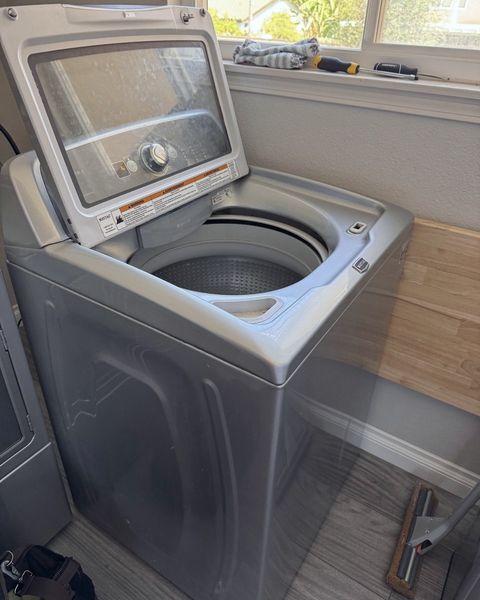 A top-load washer with its lid raised, the wash basket open inside