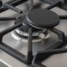 A cooktop burner under a cast-iron grate with its round cap sitting off center and the small white igniter beside it