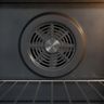 The round slotted fan cover on the back wall of an oven, behind a wire rack