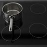 A steel saucepan sitting off center on one zone of a black glass induction cooktop